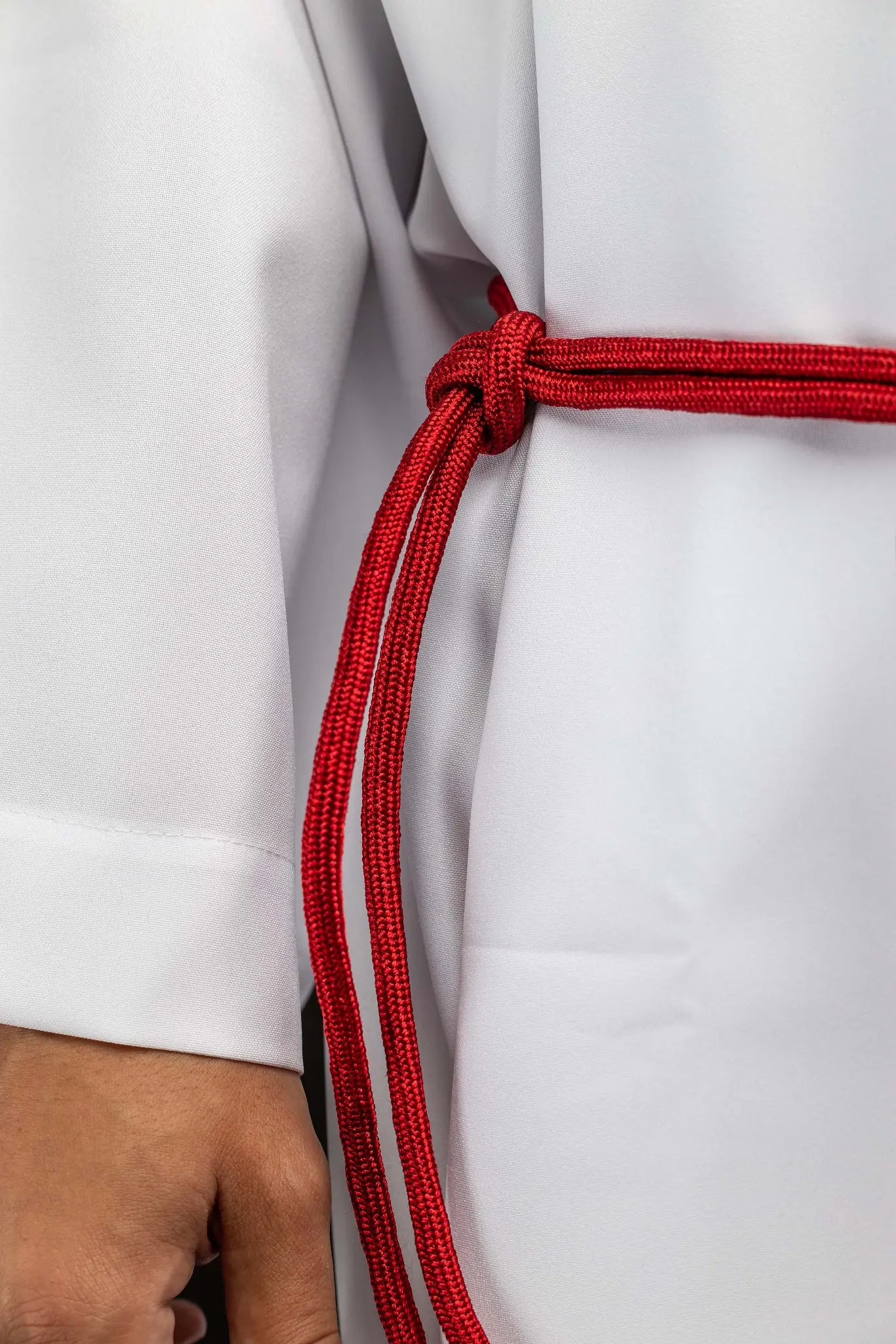 Red liturgical cincture with decorative tassels made from braided cord, tied around an alb.