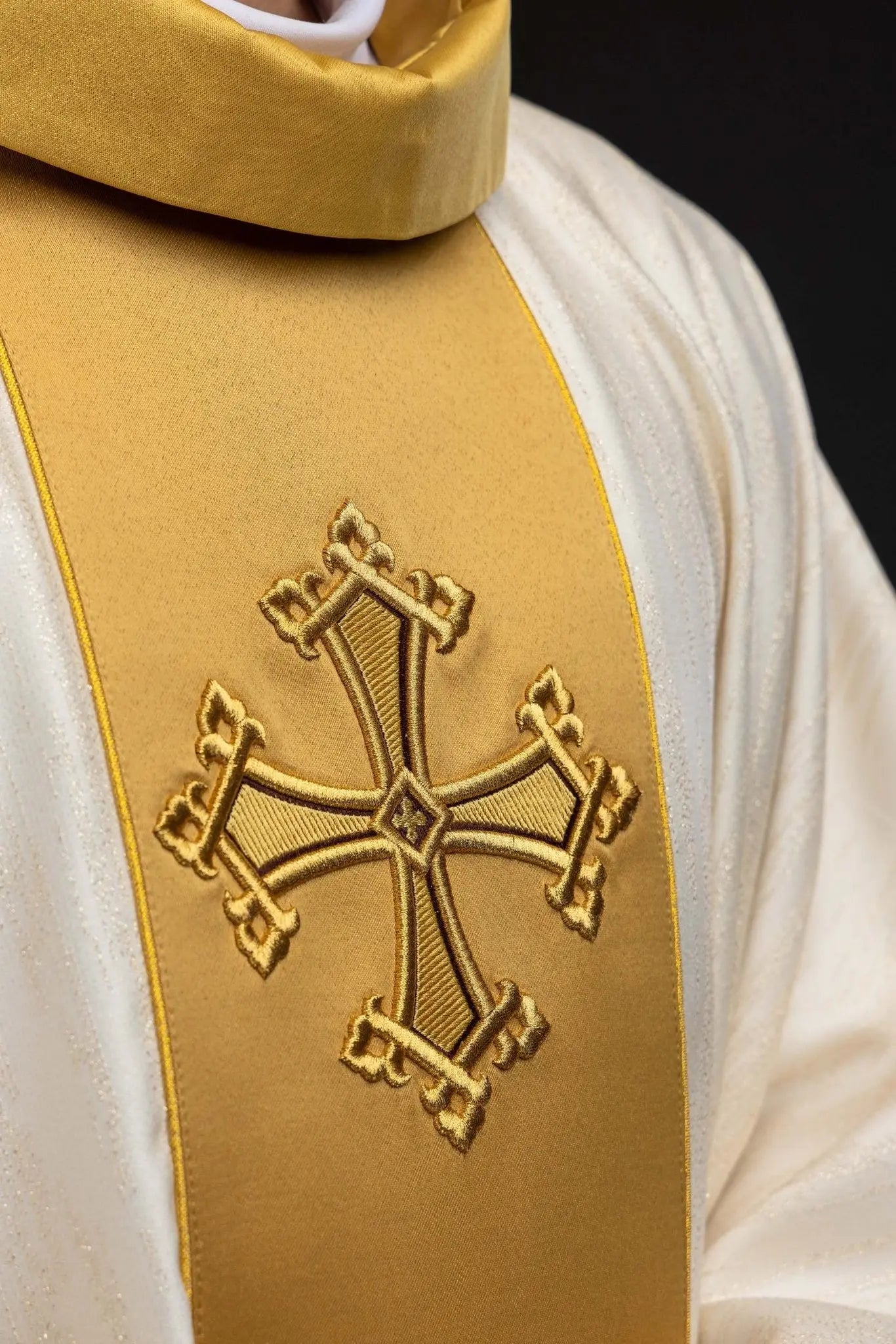 Ecru chasuble with embroidered cross motif and gold band on decorative fabric