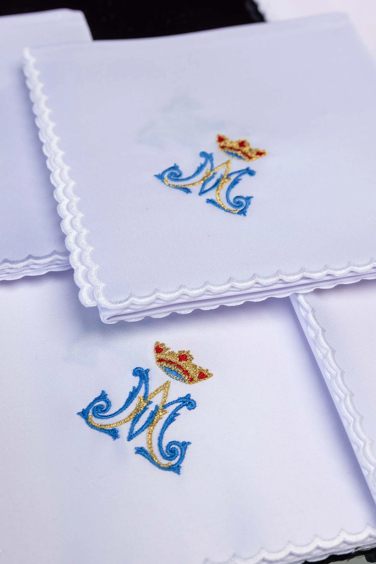 Białe korporały liturgiczne z haftem monogramu „M” i korony, zbliżenie na ułożone korporały
