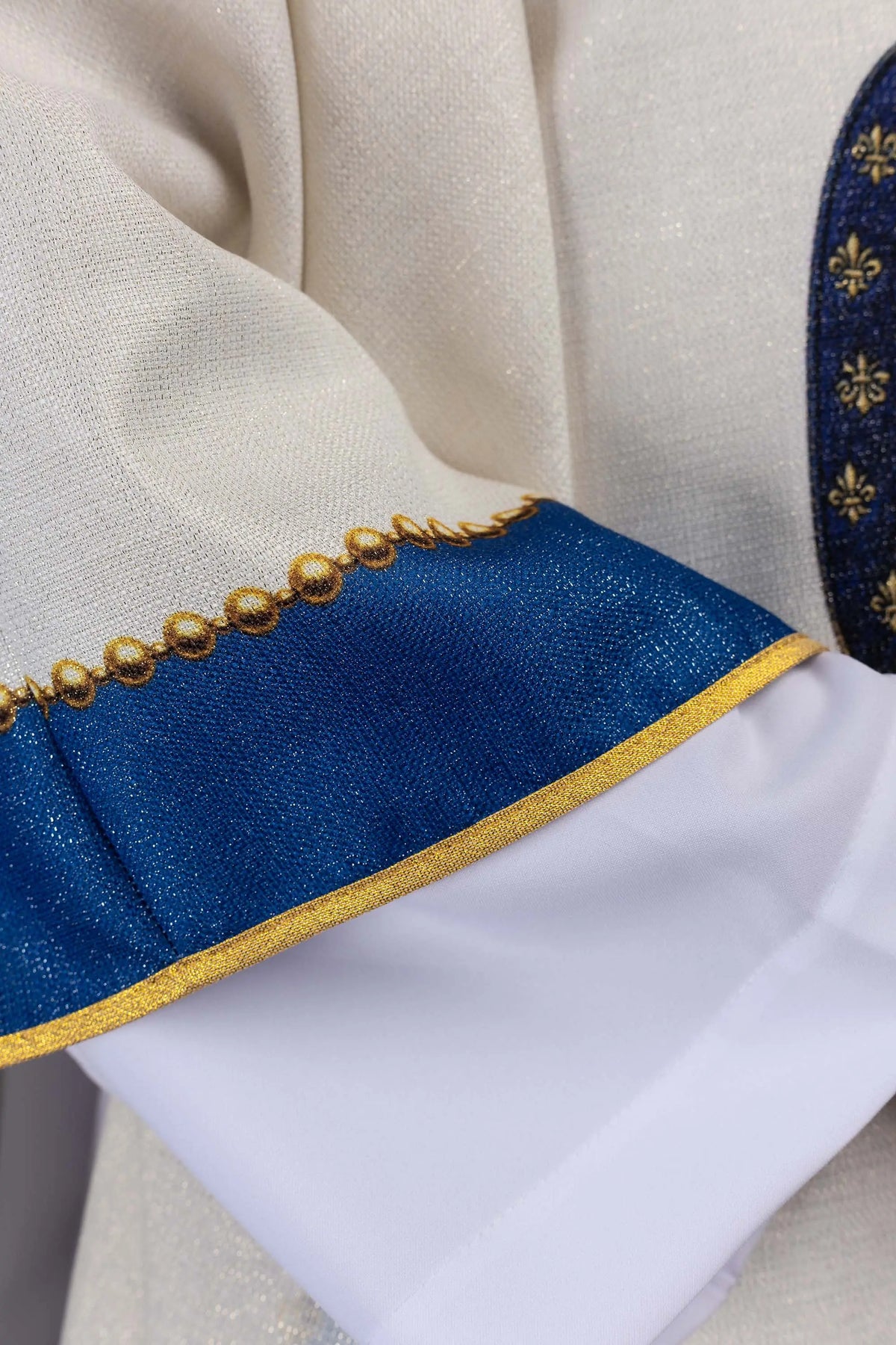 Biały ornat maryjny z niebieską lamówką i złotymi kulkami, zbliżenie rękawa