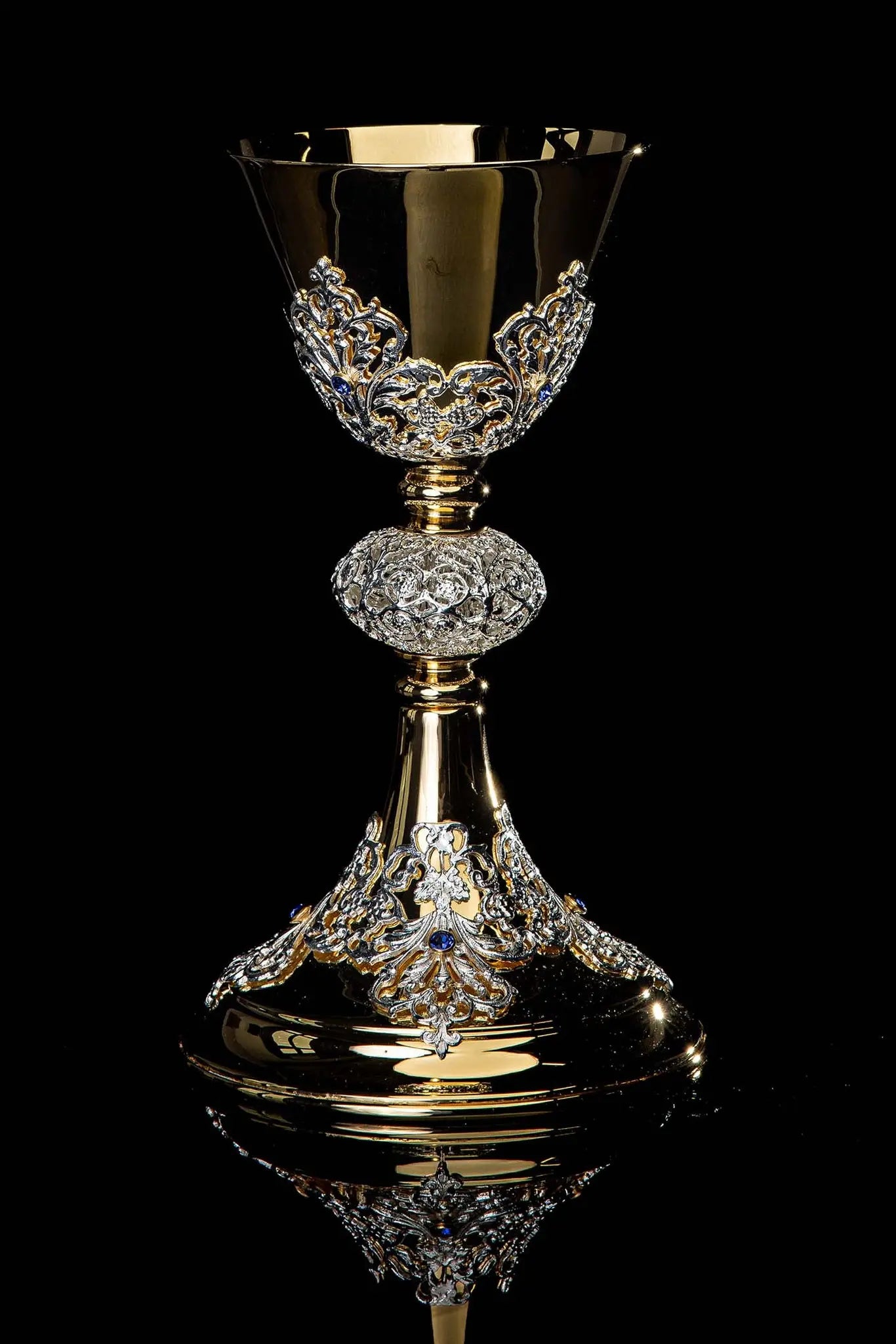 Handmade gold-plated liturgical chalice with silver-plated floral ornamentation and blue sapphire-like stones. The chalice features a decorated cup, nodus, and base.