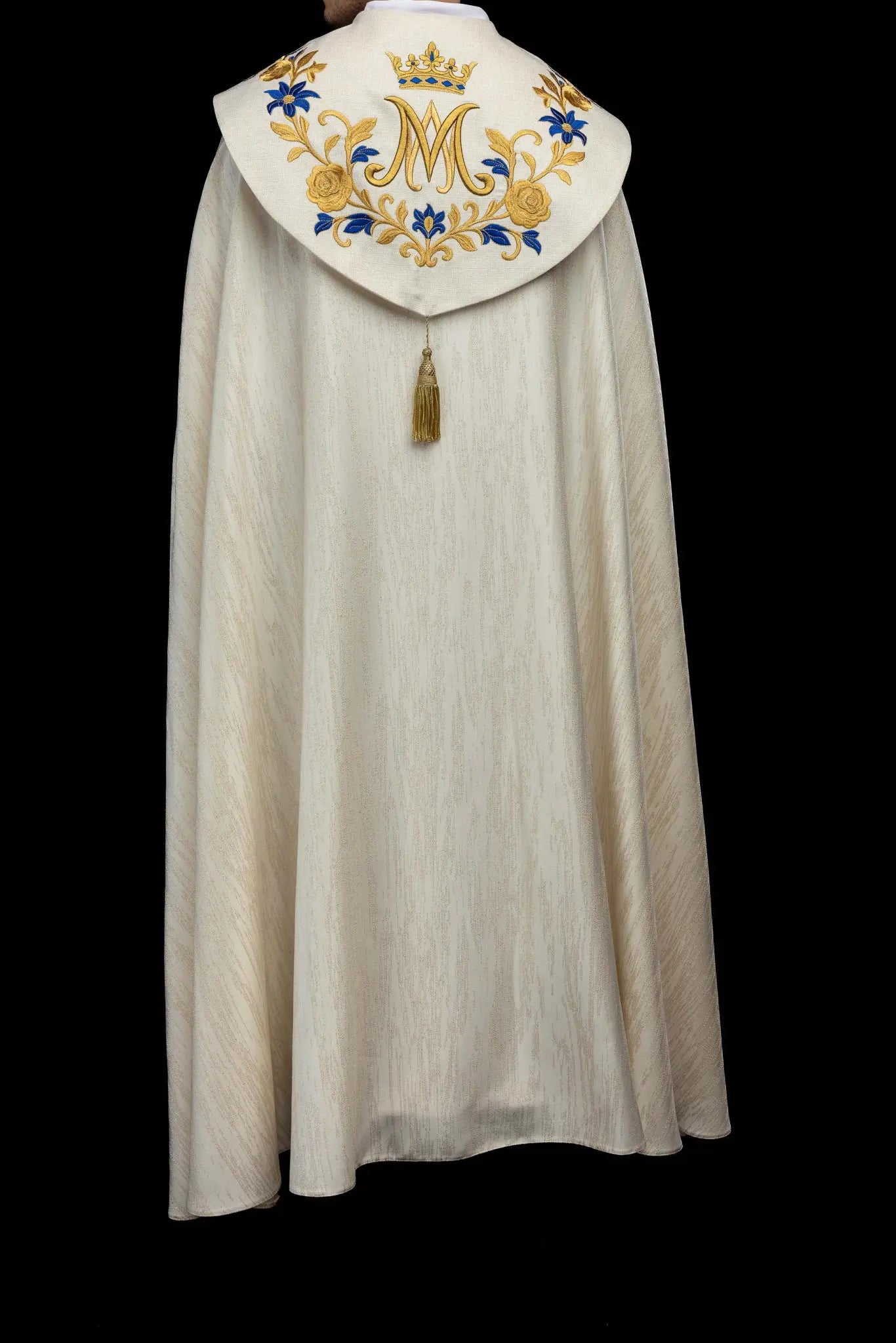 Ecru embroidered cope with Marian symbol, featuring gold and blue floral embroidery, a crowned 'M' monogram, and an ornate gold clasp with chain.