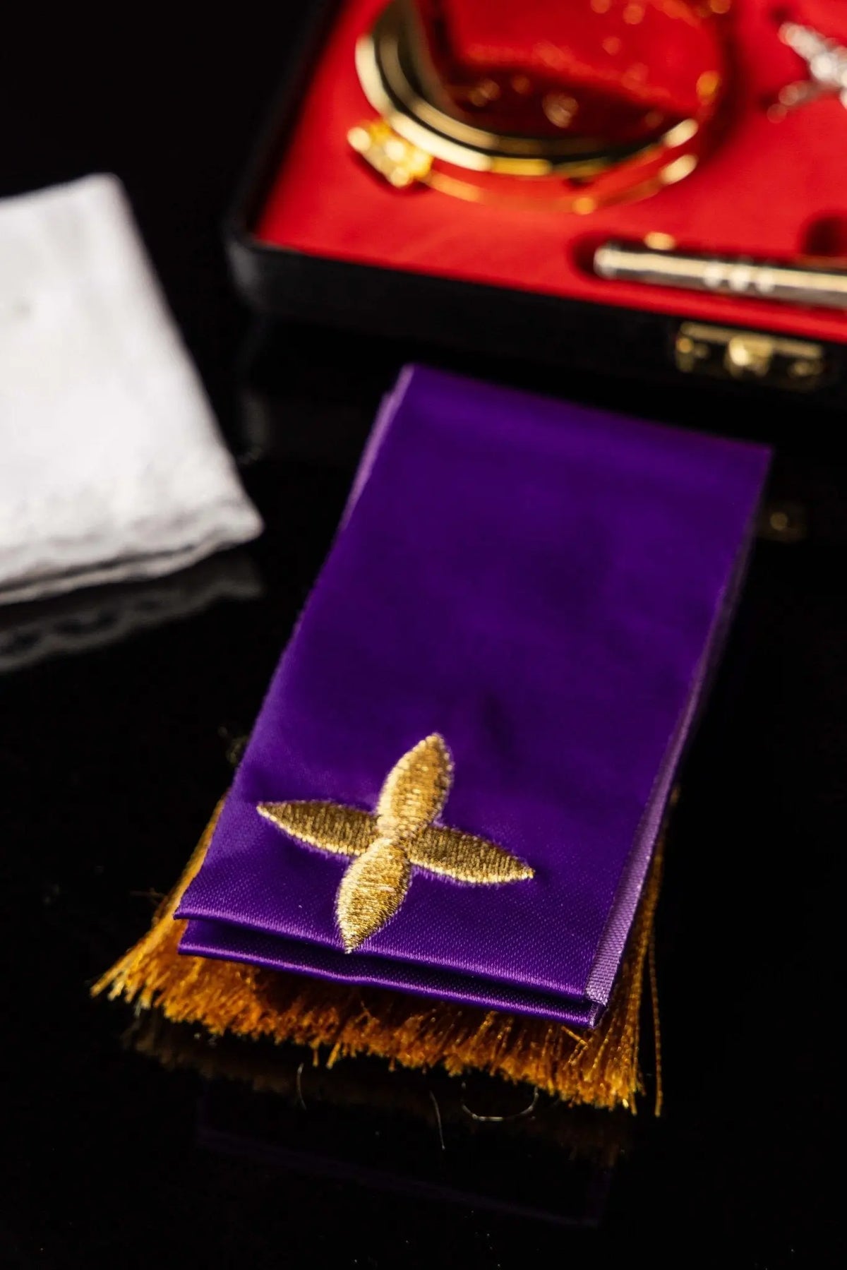 Fioletowa bursa liturgiczna z haftowanym złotym krzyżem i frędzlami, zbliżenie