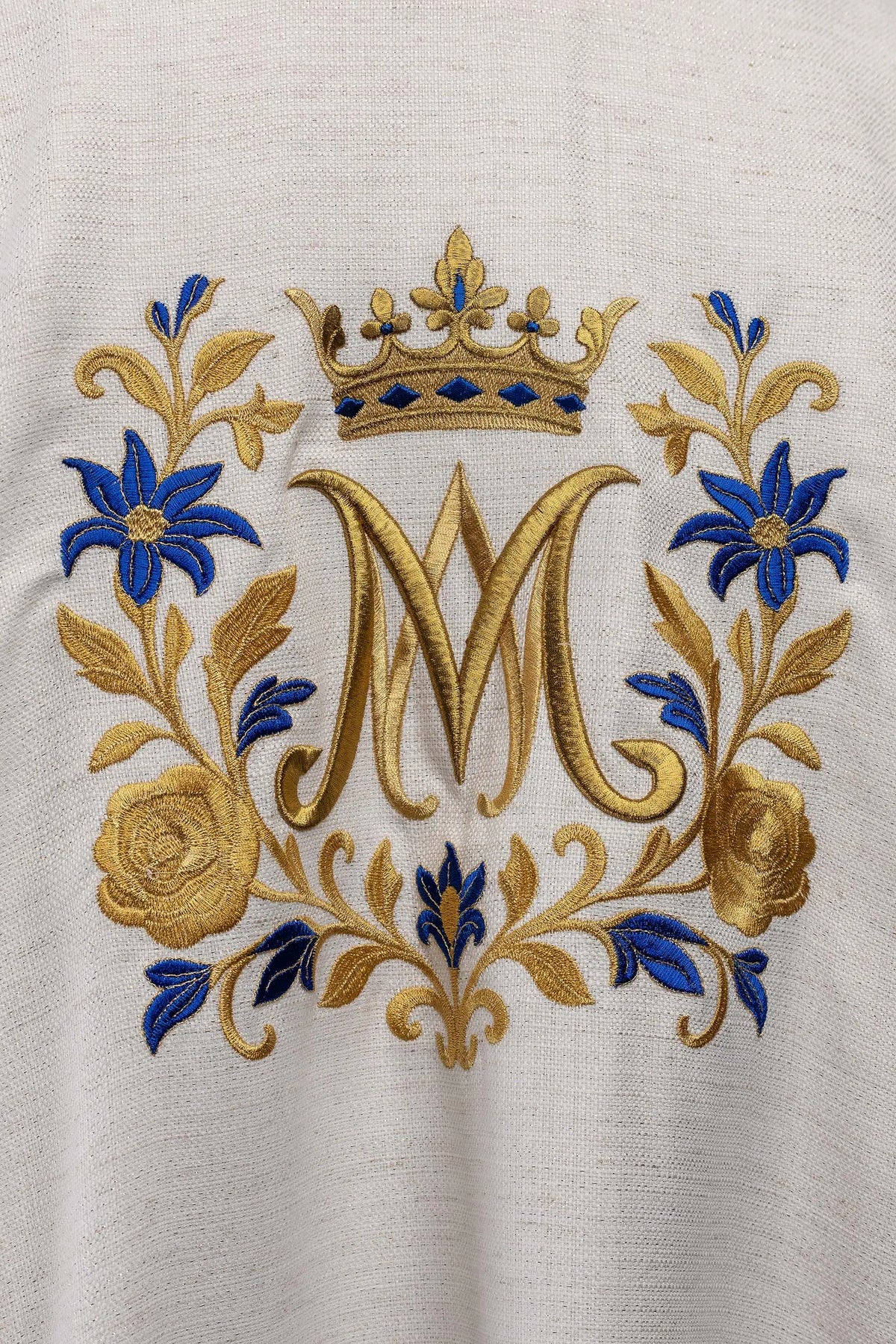 Biała dalmatyka z monogramem „M” i koroną, zbliżenie haftu