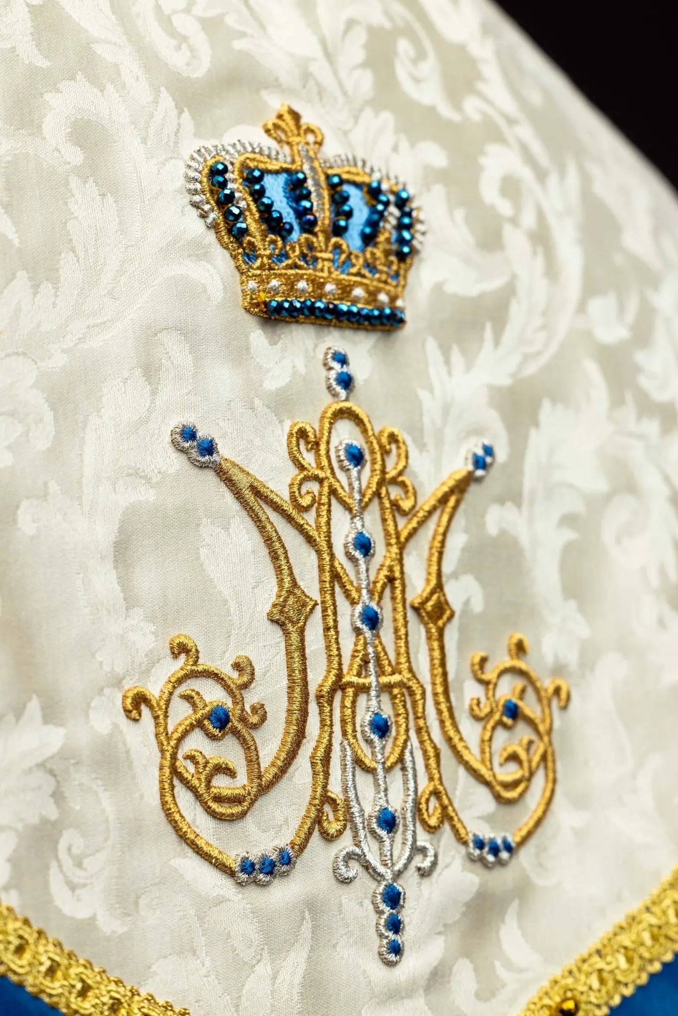 Ecru Marian cope with natural stones and blue velvet trim, part of the Handmade Collection, featuring an ornate metal clasp and gold tassel.